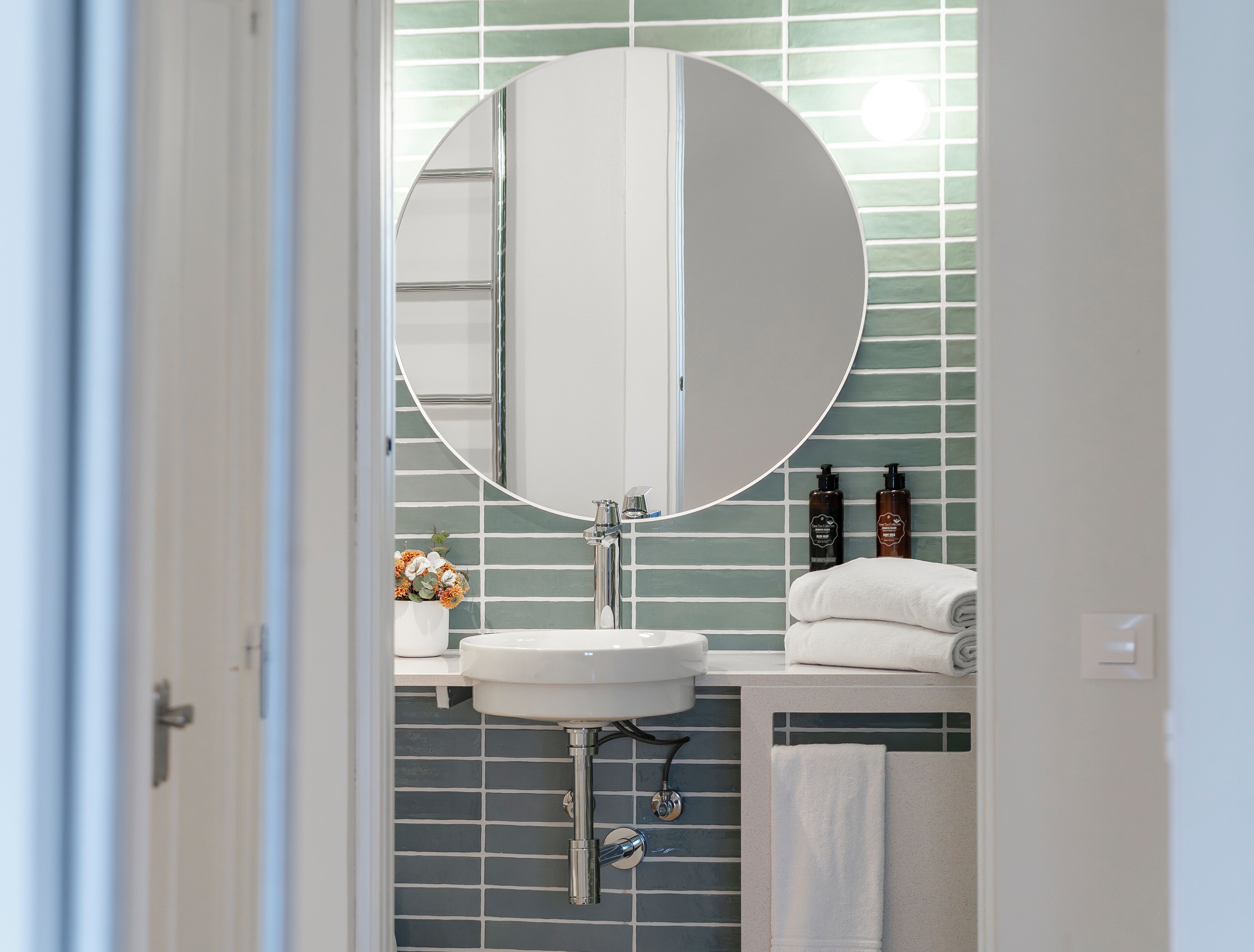 A bathroom with a round mirror, white sink, and tiled backsplash.