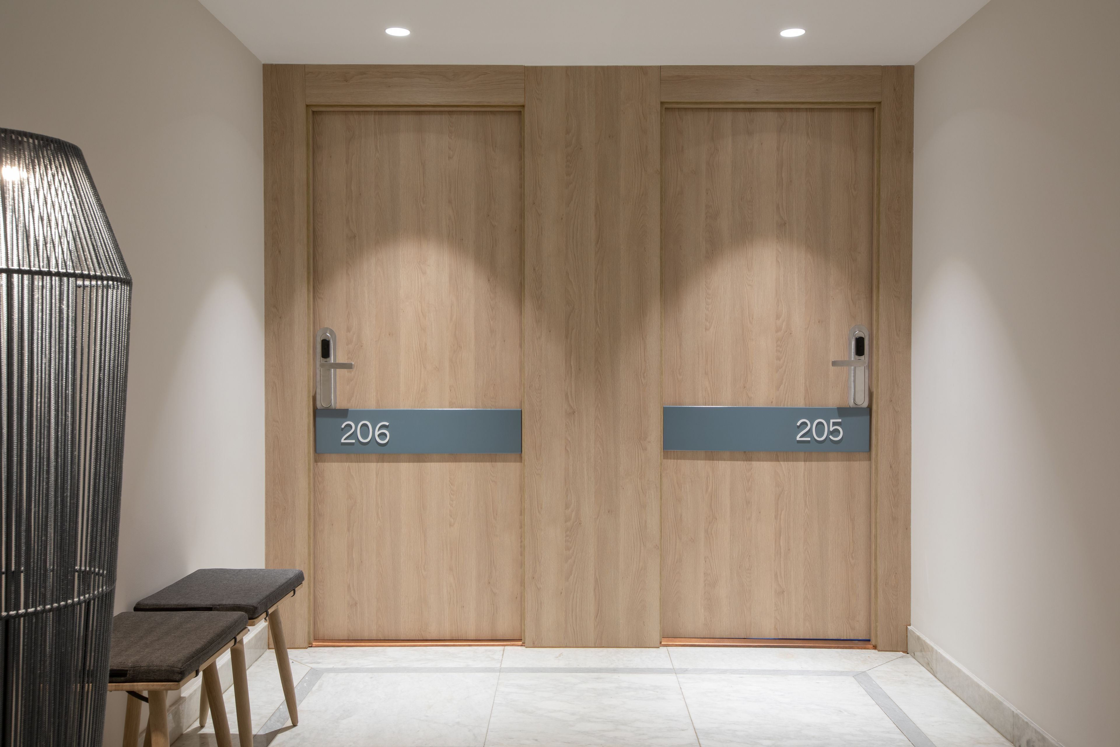 Un couloir avec deux portes en bois portant les numéros 206 et 205, un banc et un luminaire moderne.