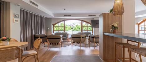 A modern hotel room with a dining area, seating, and a view through large windows.
