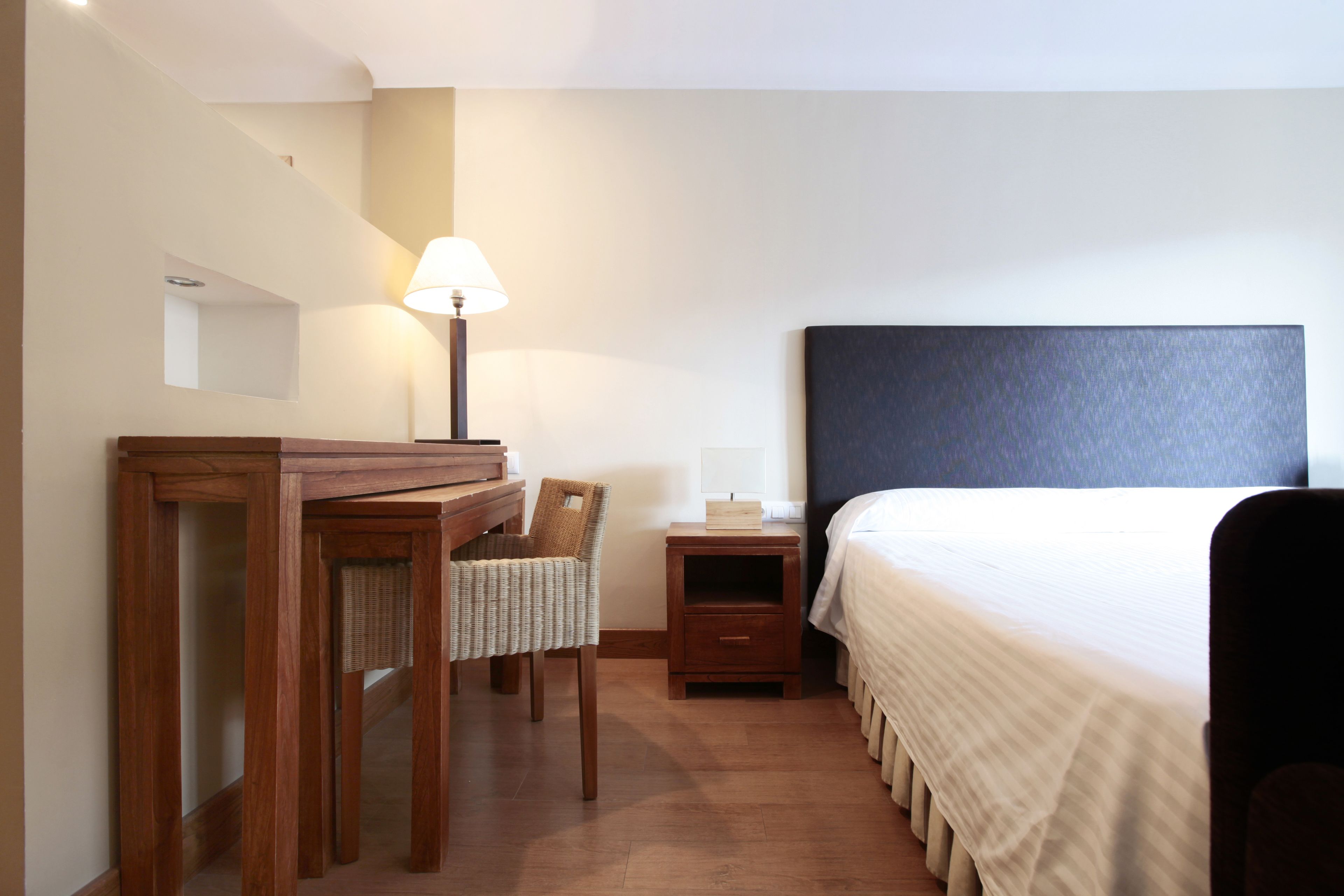 Una habitación de hotel con una cama, un escritorio con una silla, una mesita de noche y una lámpara.