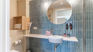 Een moderne badkamer met een wit wastafelmeubel, blauwe wandtegels, een houten plank met handdoeken, een toilet en een prullenbak.