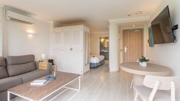 A modern hotel room with a sofa, a small table, a bed, a bathroom, and a TV mounted on the wall.