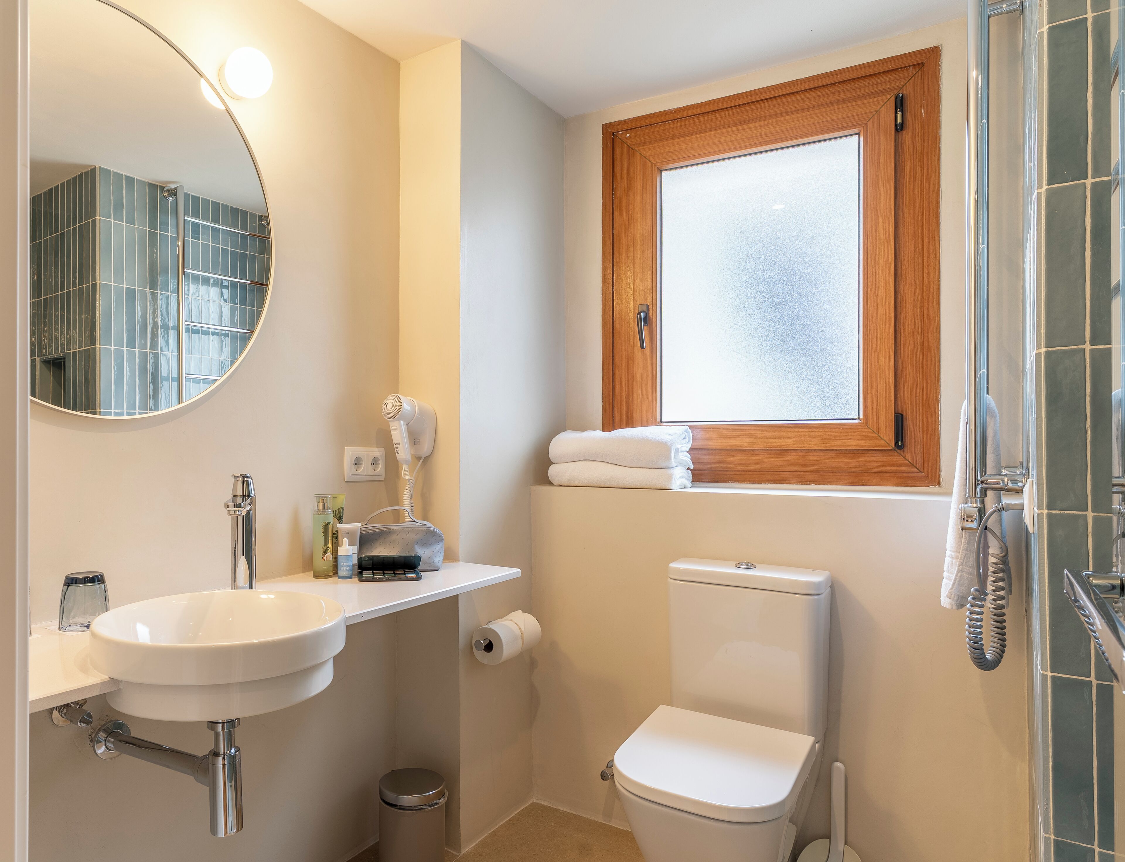 A bathroom with a white sink, a mirror, a toilet, a window, and a shower area.