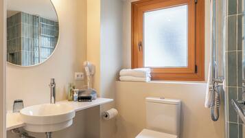 Un baño con lavabo blanco, espejo, inodoro, ventana y zona de ducha.