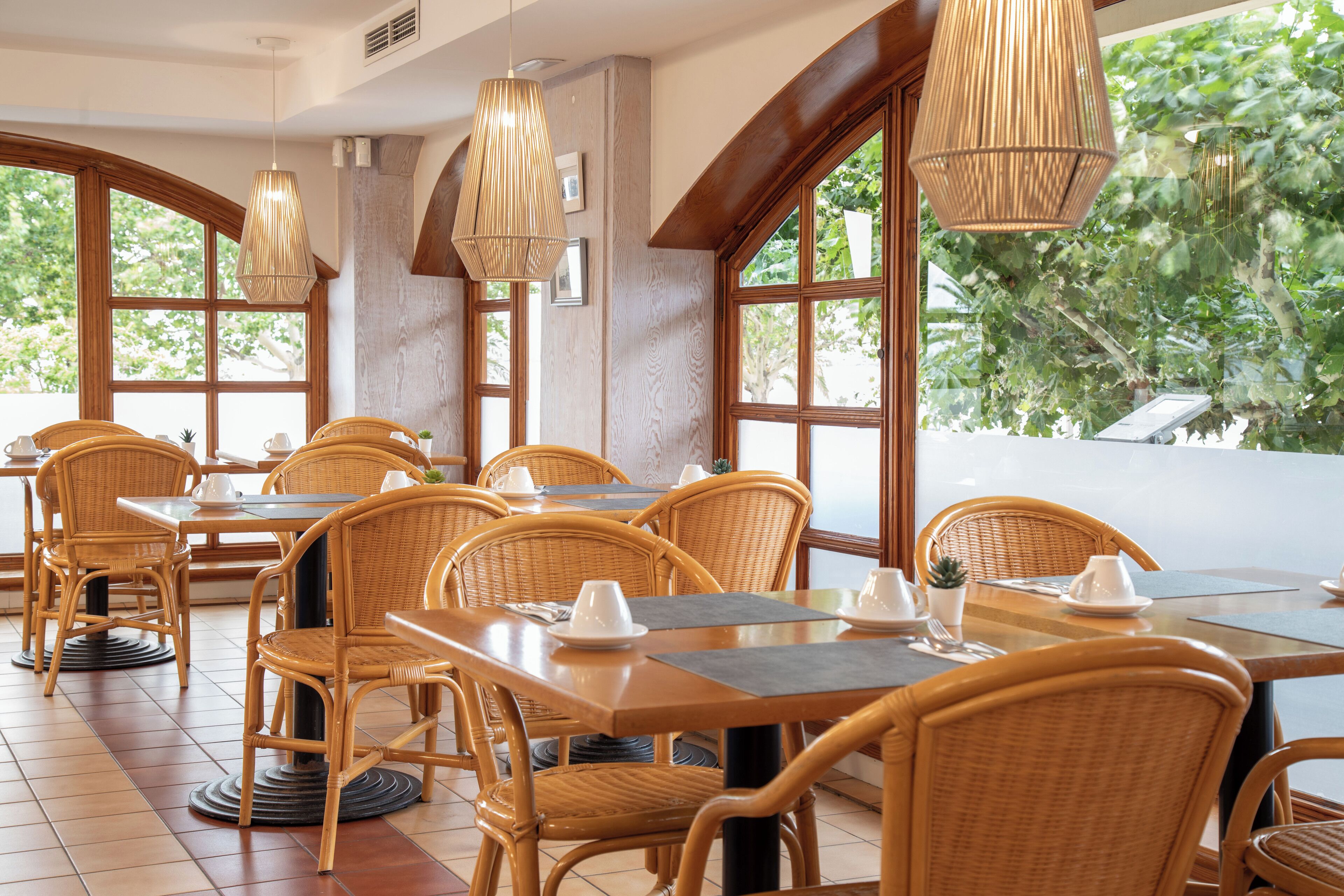 Un restaurante con mobiliario de mimbre, ventanas amplias y lámparas colgantes.