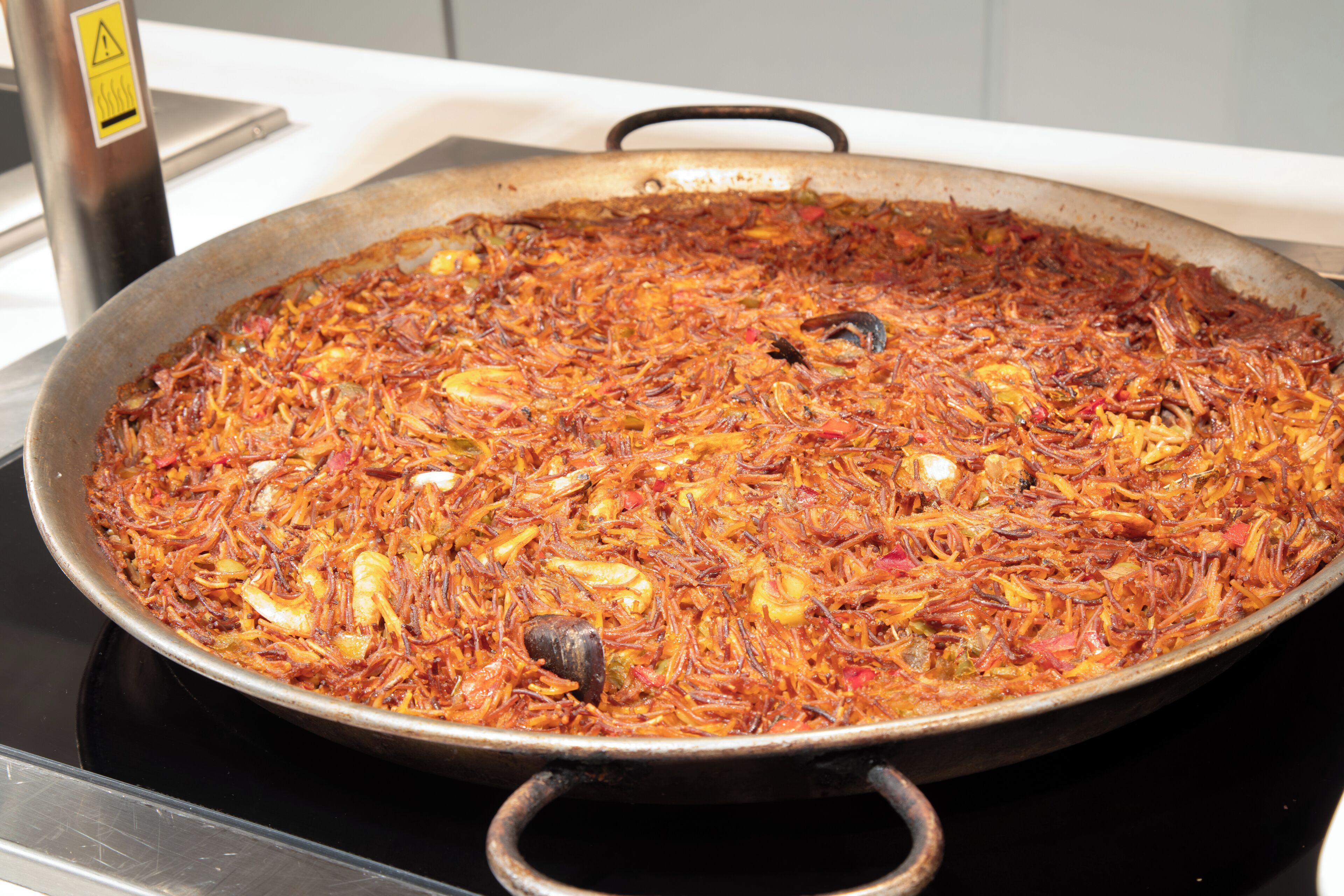 A large, shallow cooking pan filled with a seafood dish, placed on a stove.