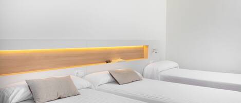 Habitación de hotel con dos camas individuales, cabecera de madera y mesita de noche con lámpara.