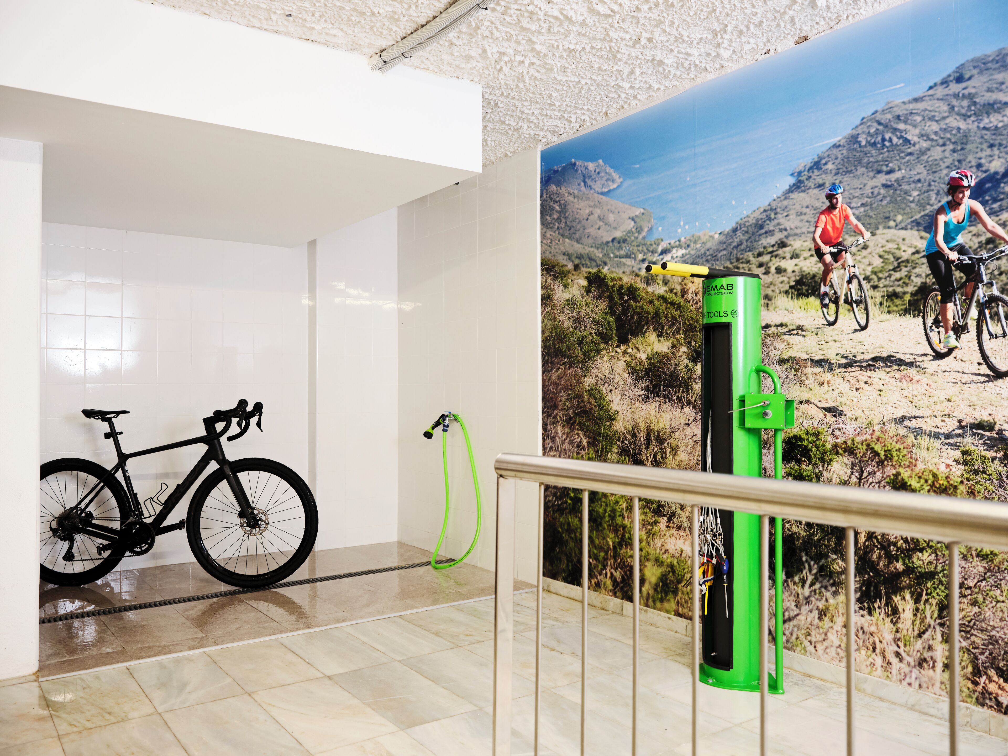A room with a bicycle, a green water dispenser, and a mural of cyclists on a mountain trail.