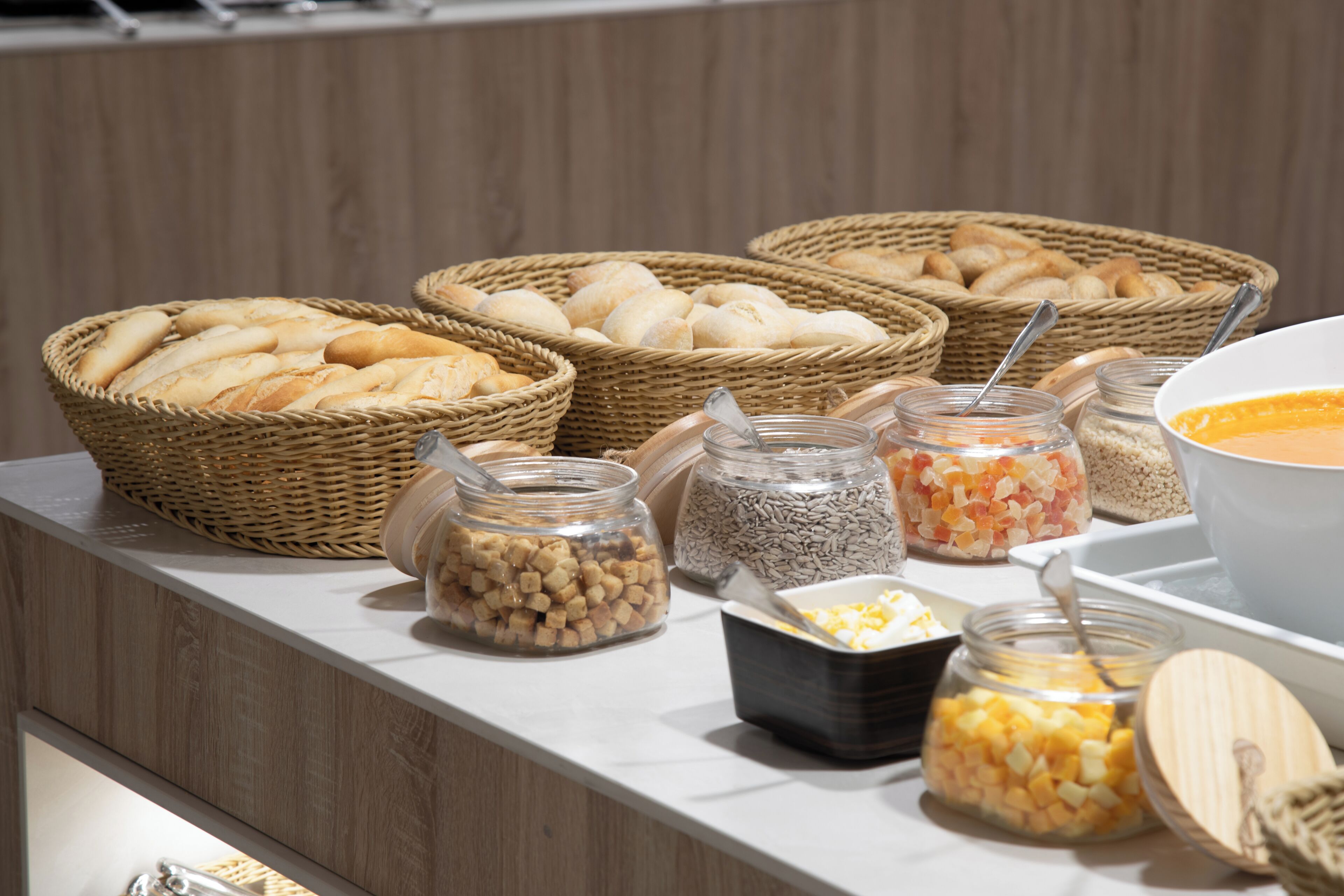 Une table de buffet avec des paniers de pain, des bocaux de noix et un saladier de soupe.
