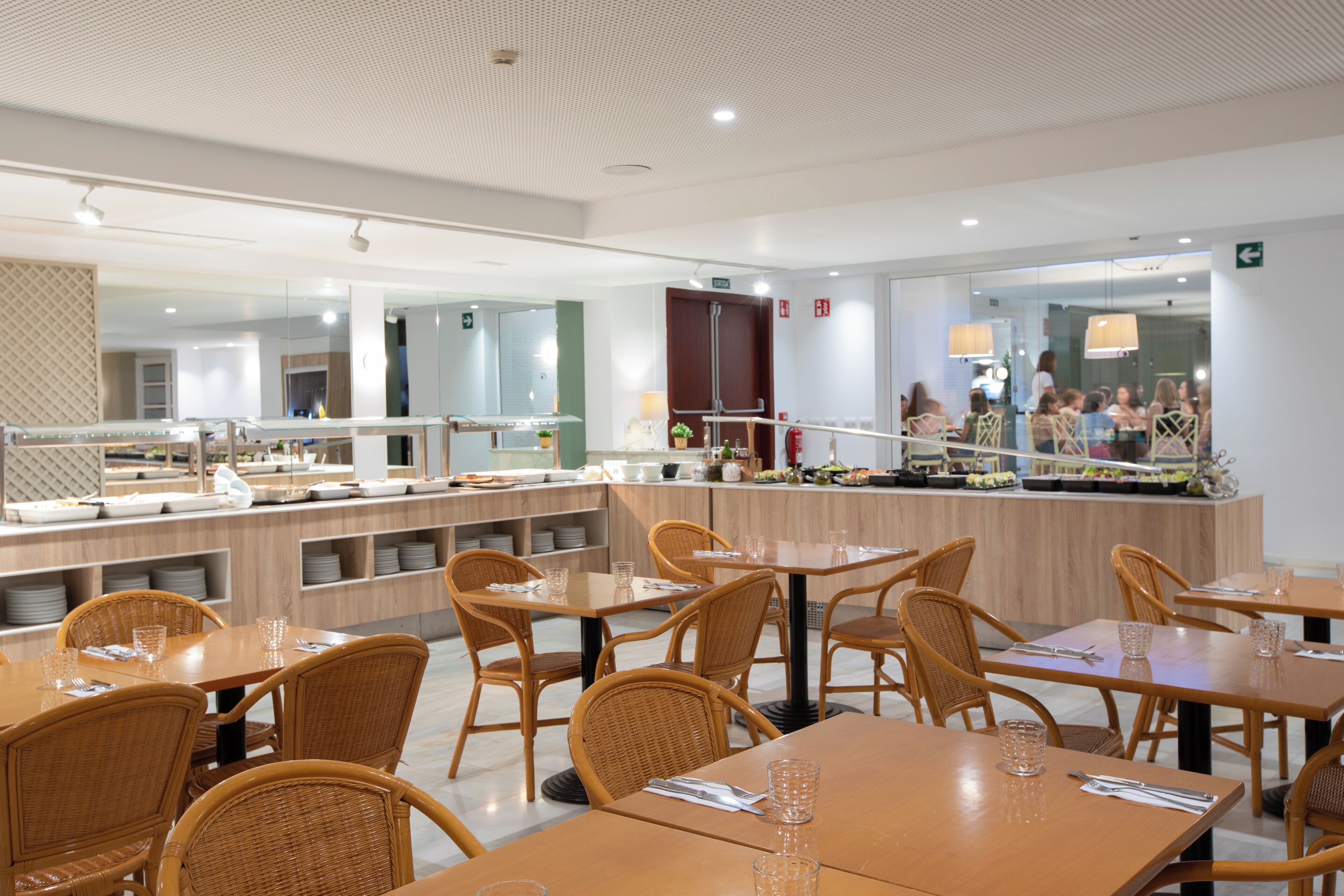 Un restaurant moderne avec des tables et des chaises en bois, un espace buffet et une vue sur la salle à manger grâce à une cloison en verre.