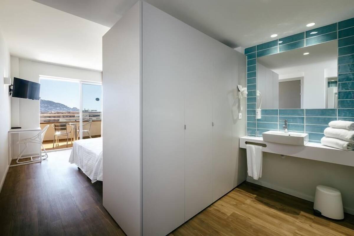 A modern hotel room with a balcony, a large mirror, and a white vanity with a sink.