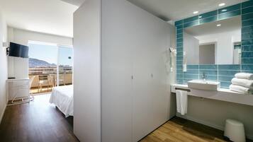 Une chambre d’hôtel moderne dotée d’un balcon, d’un grand miroir et d’une coiffeuse blanche avec un lavabo.