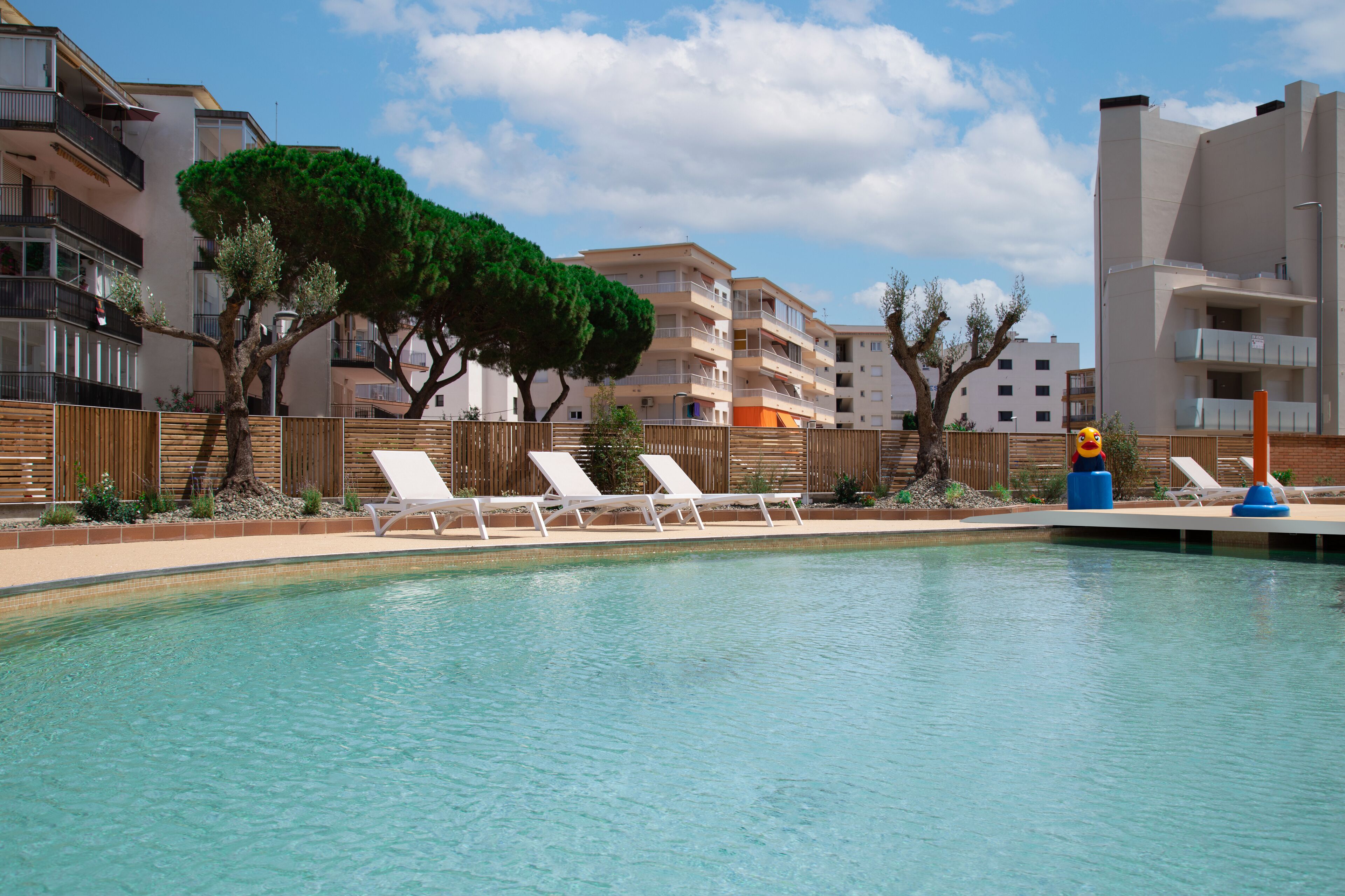 A swimming pool with white lounge chairs and a wooden fence.