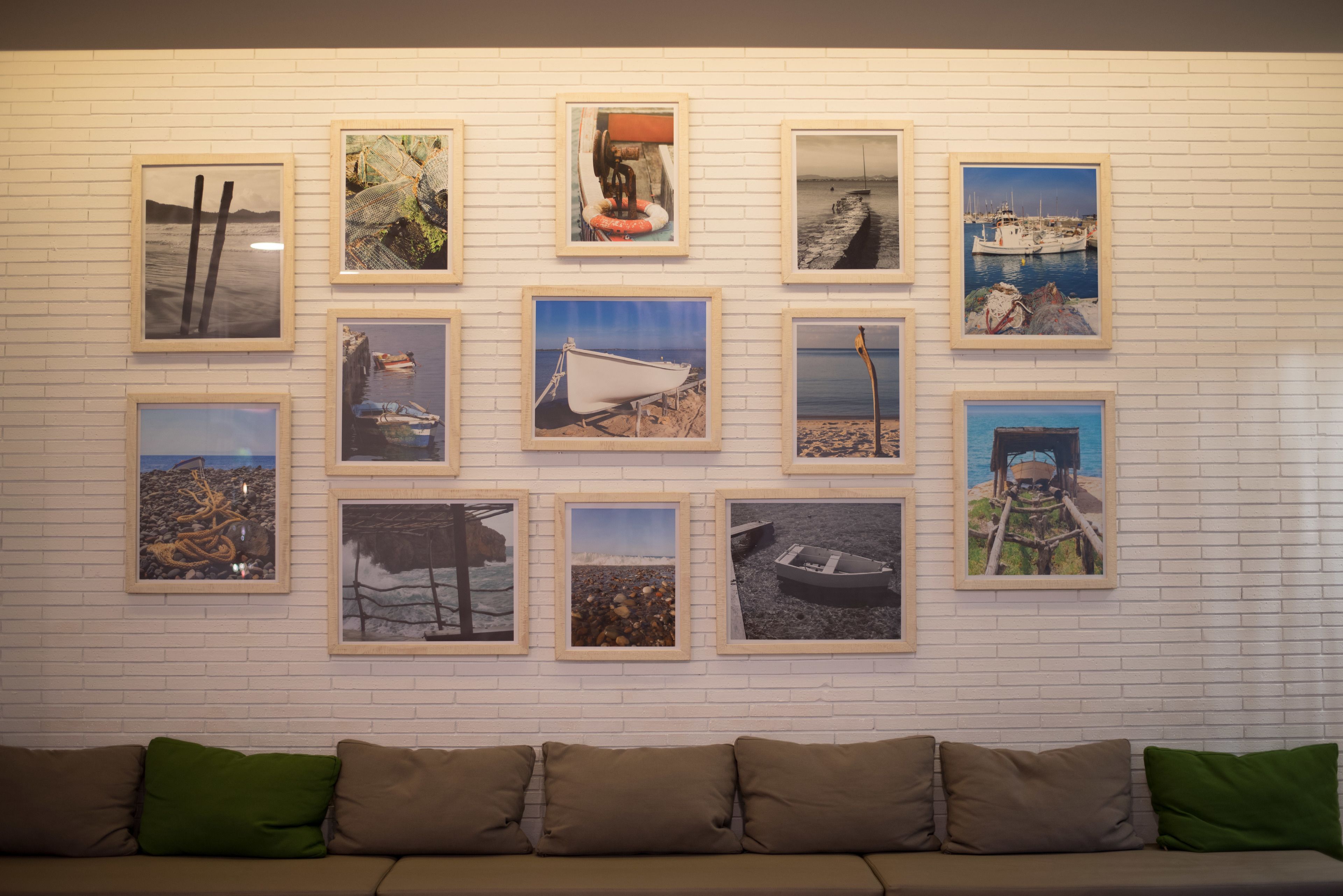 A wall with framed pictures of coastal scenes, a white brick wall, and a sofa with green cushions.