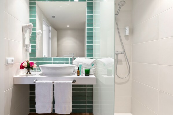 Un baño con un lavamanos blanco, un espejo, una ducha y dos toallas colgadas en un perchero.