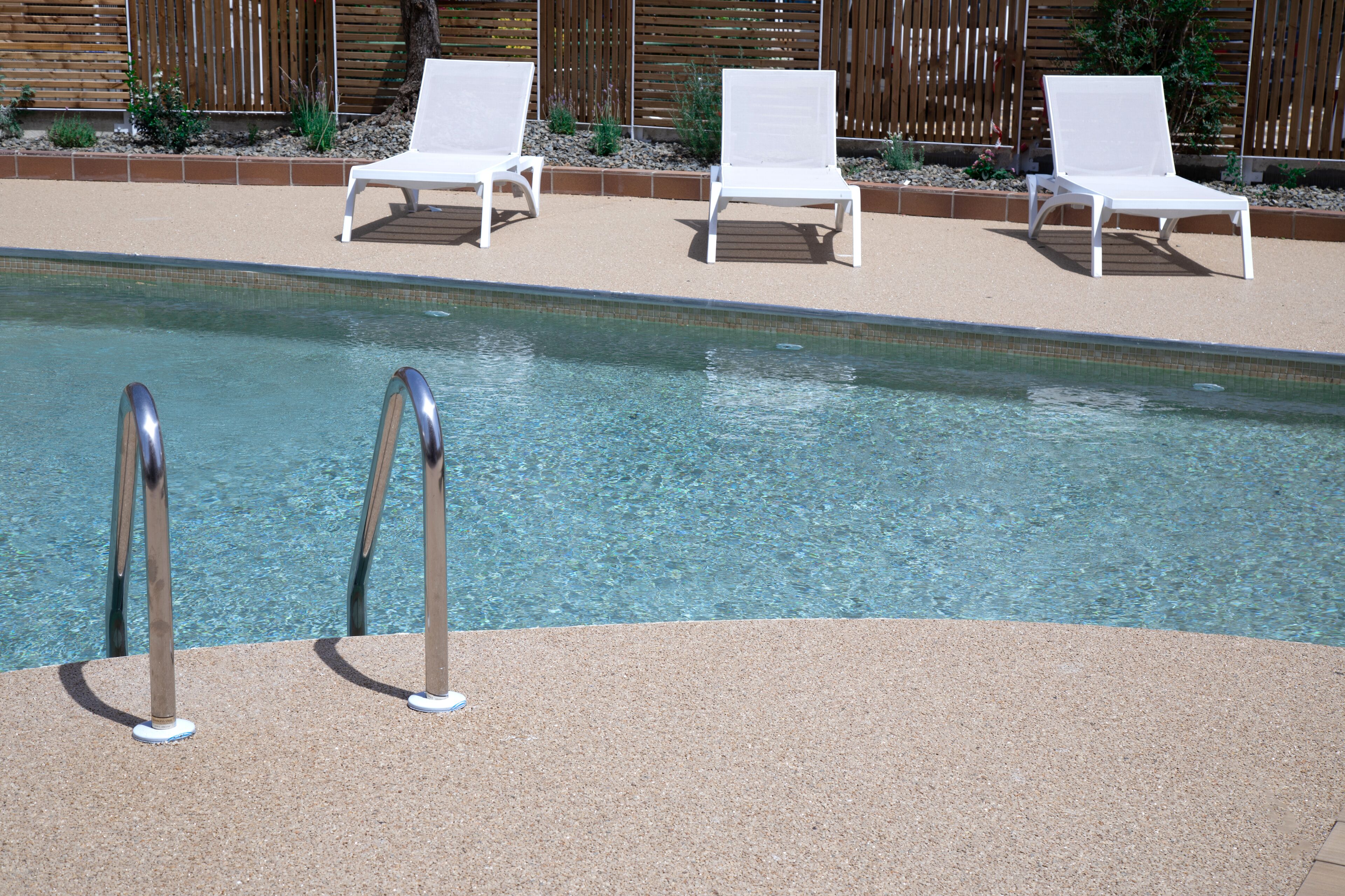 Una piscina amb aigua cristal·lina, dues escales metàl·liques i tres gandules blanques.