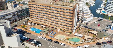 A multi-story hotel with a rooftop pool, a marina with boats, and a parking area.