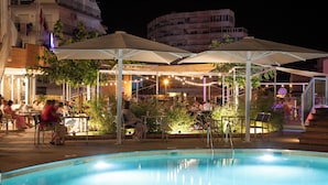 An outdoor pool area with umbrellas, seating, and string lights. - Hotel Prestige Sant Marc (Roses)