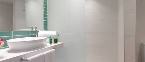 A modern bathroom with a white sink, green-tiled shower, and a large mirror.