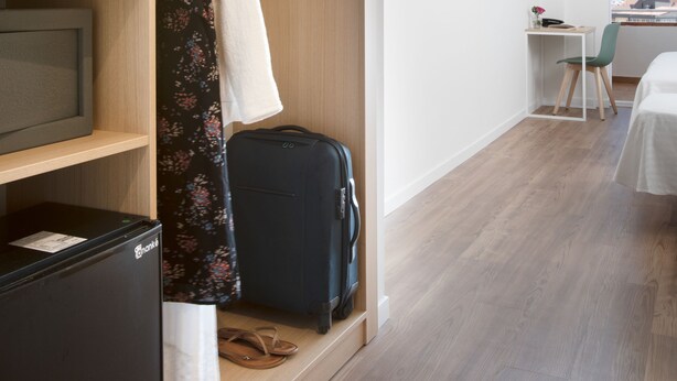 A modern hotel room with a wooden wardrobe, a television, a desk with a chair, and a view of the city. - Hotel Prestige Sant Marc (Roses)