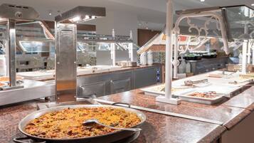 A buffet setup with a large pan of food, serving utensils, and various food containers on a granite countertop.