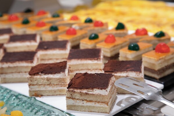 Una bandeja de postres cuadrados con varias capas, algunos coronados con esferas de gelatina de colores, y una espátula metálica para servir a un lado.
