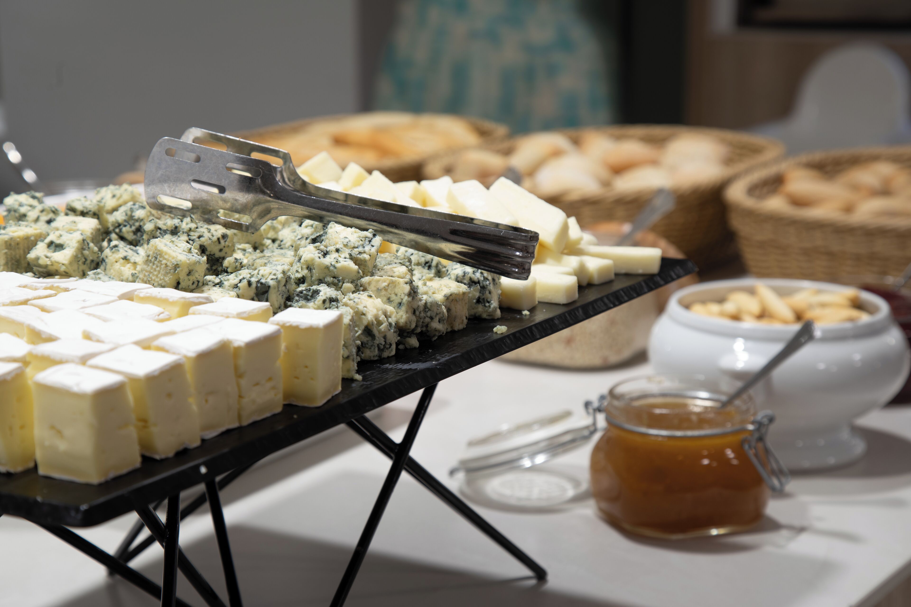 A buffet table with various cheeses and a jar of jam.