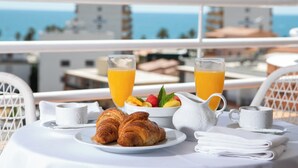 A breakfast table with croissants, fruit, and orange juice on a balcony overlooking the sea. - Hotel Prestige Sant Marc (Roses)