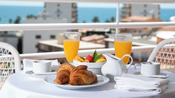A breakfast table with croissants, fruit, and orange juice on a balcony overlooking the sea. - Hotel Prestige Sant Marc (Roses)