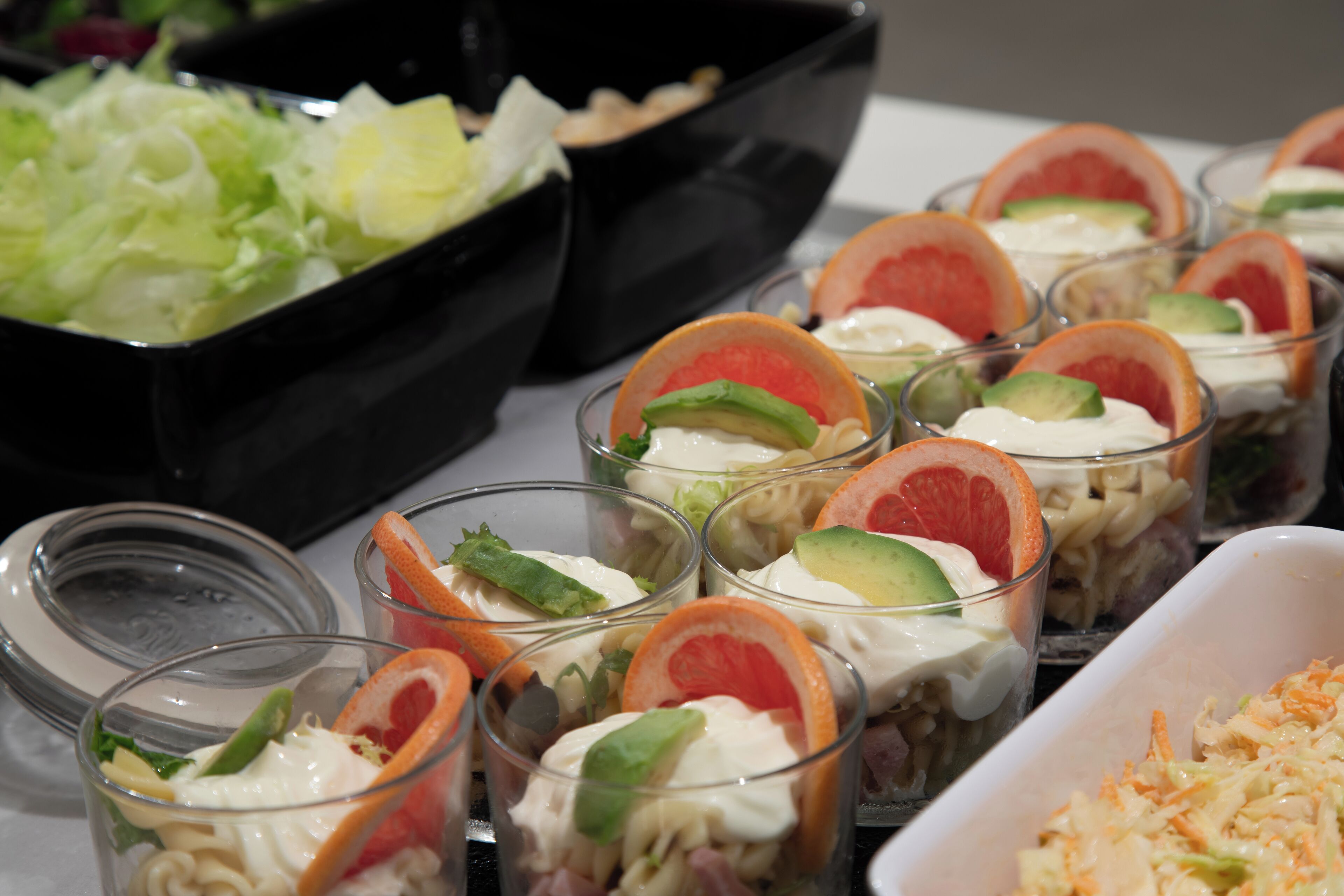 A buffet with various dishes including salads, coleslaw, and layered desserts in clear glasses.