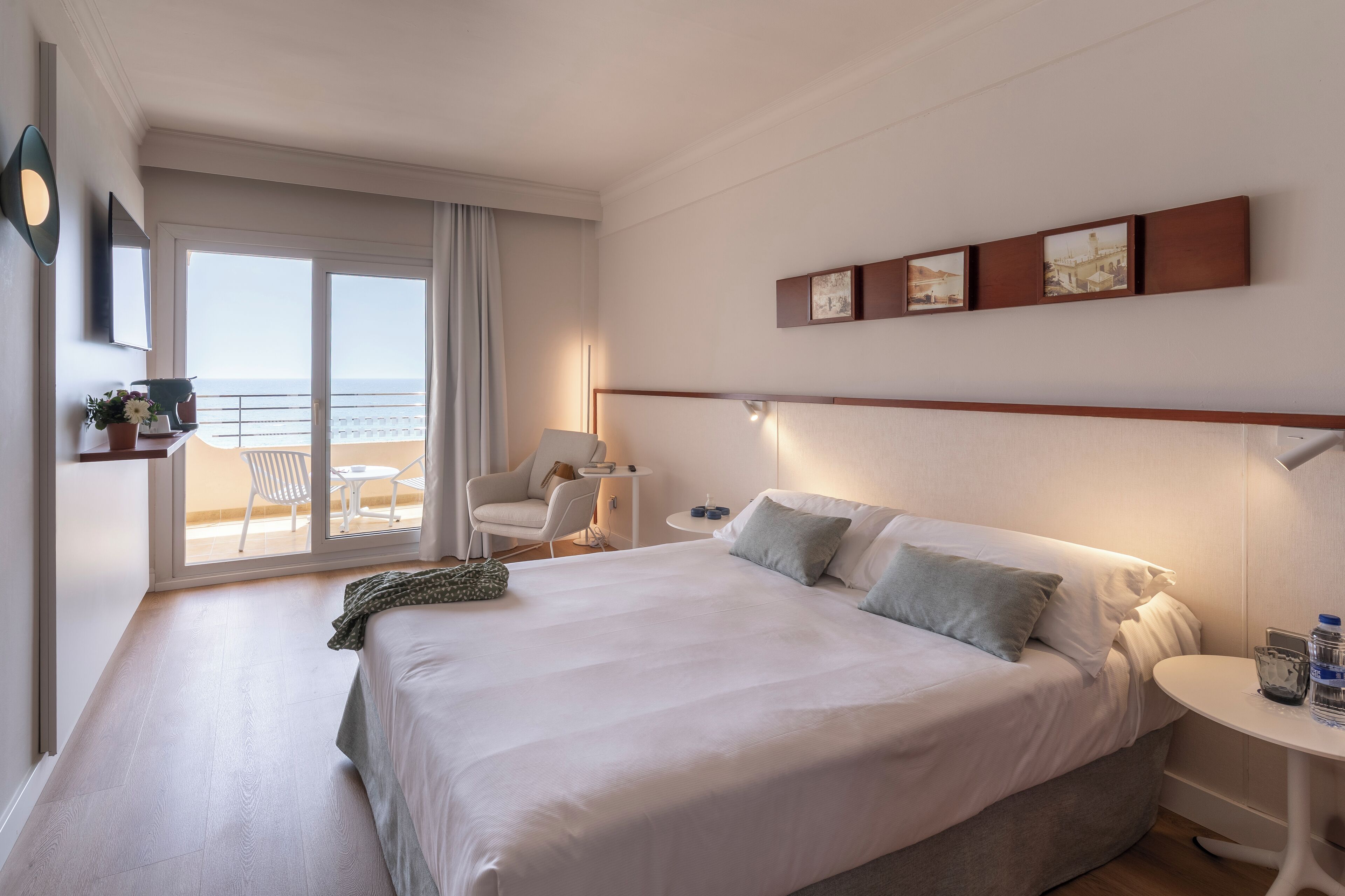Habitación de hotel con una cama grande, una mesita, una silla y vistas al mar a través de una puerta corrediza.