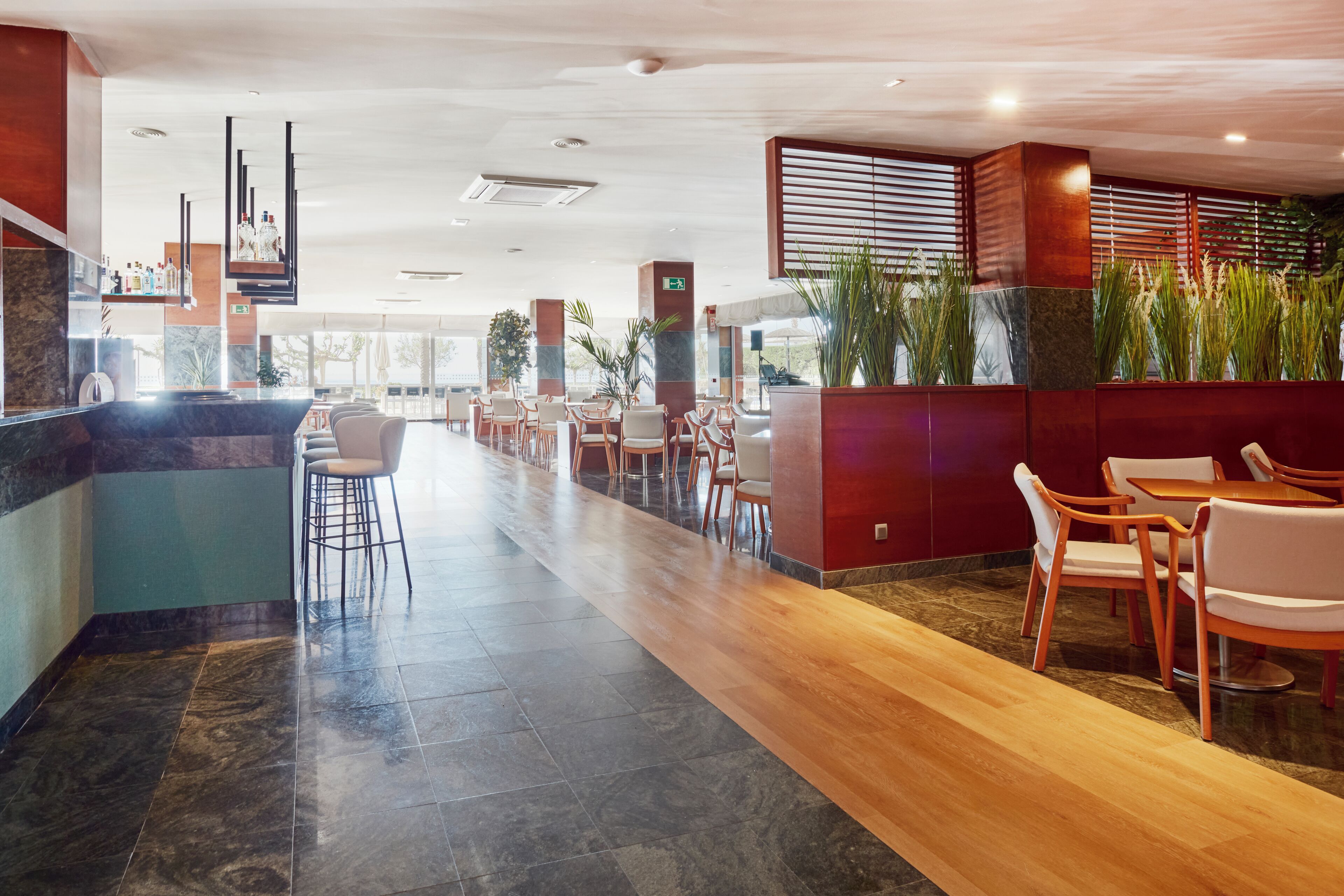 A modern hotel lobby with a long reception desk, seating area, and a bar.
