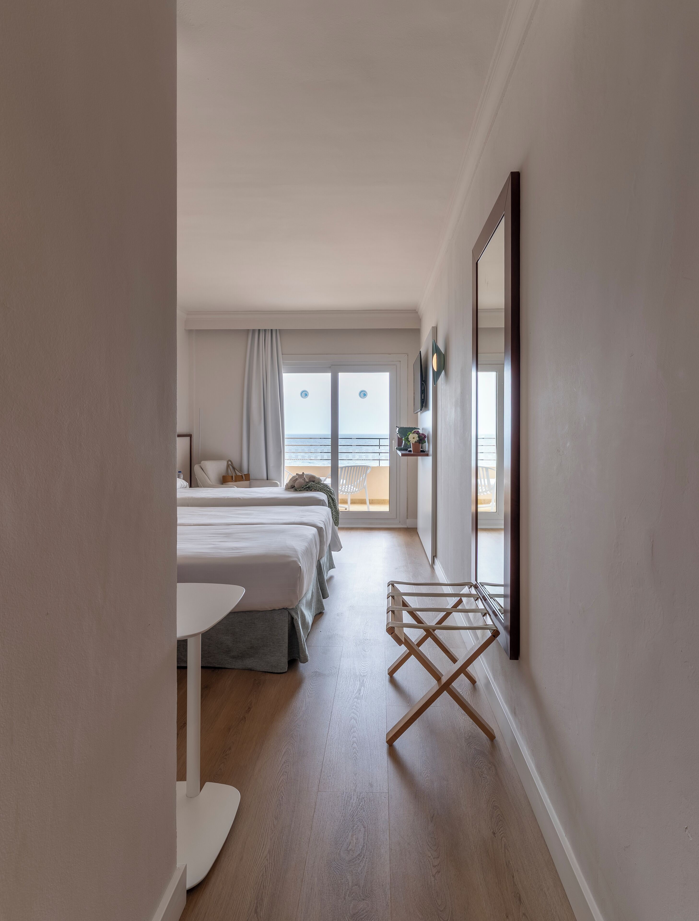 Habitación de hotel con dos camas, una mesita, una silla y un balcón con vistas al mar.