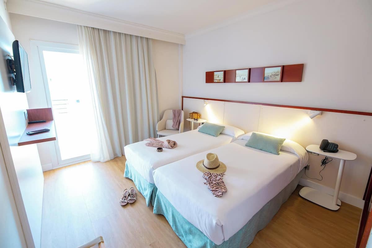 A hotel room with two beds, a desk with a chair, a TV, a phone, and a window with curtains.