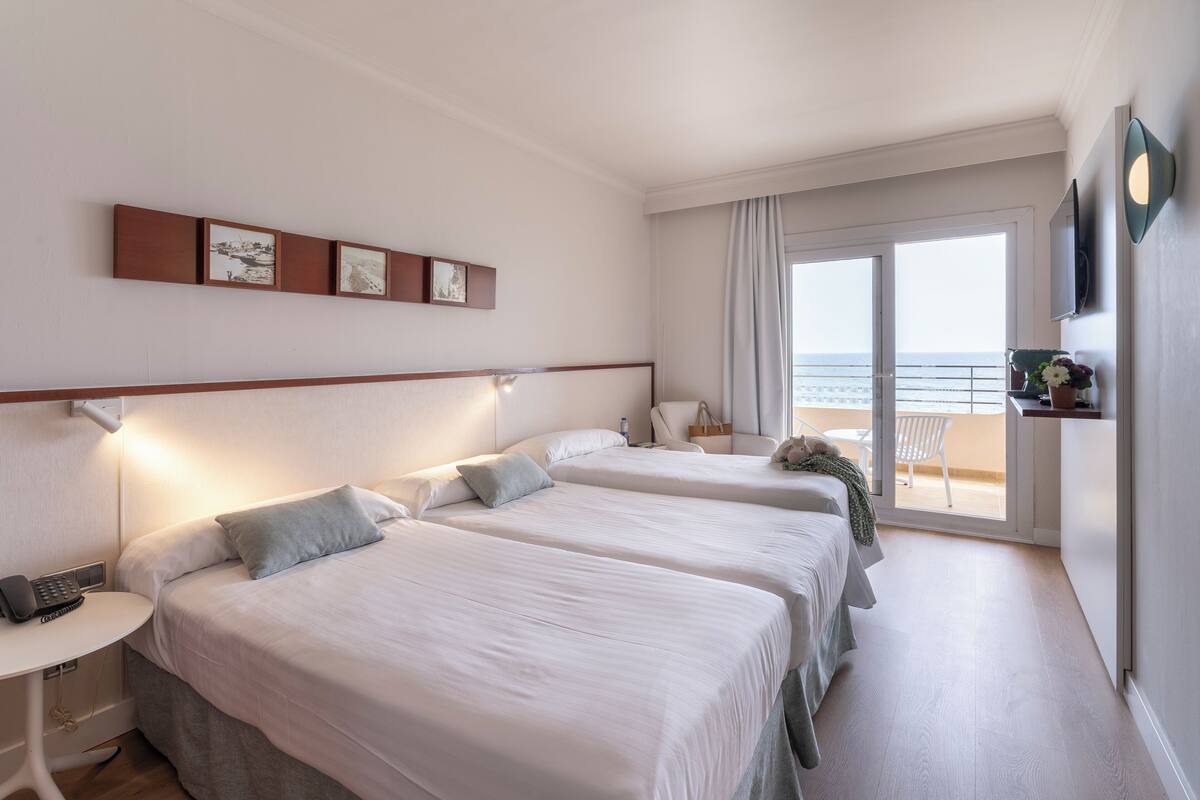 Une chambre d’hôtel avec deux lits, un bureau avec un téléphone et un balcon donnant sur la mer.