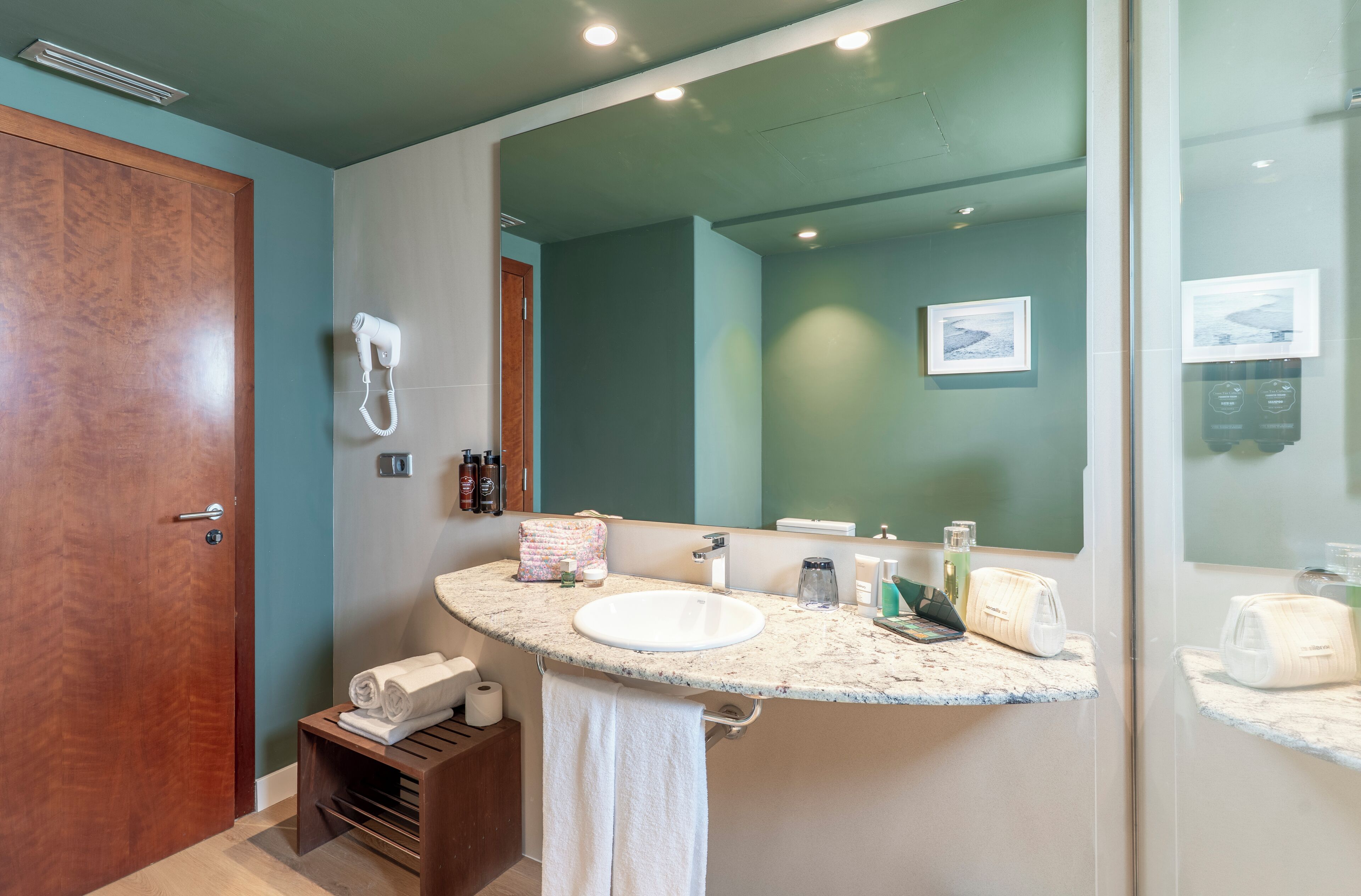 Un baño con lavamanos, espejo, toallero y secador de pelo.
