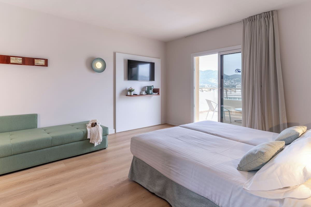 Une chambre d’hôtel moderne avec un grand lit, un canapé vert, une télévision et un balcon avec vue.