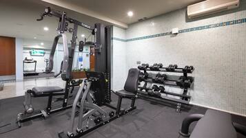 Un gimnasio con equipo de levantamiento de pesas, bancos y una estructura con mancuernas.