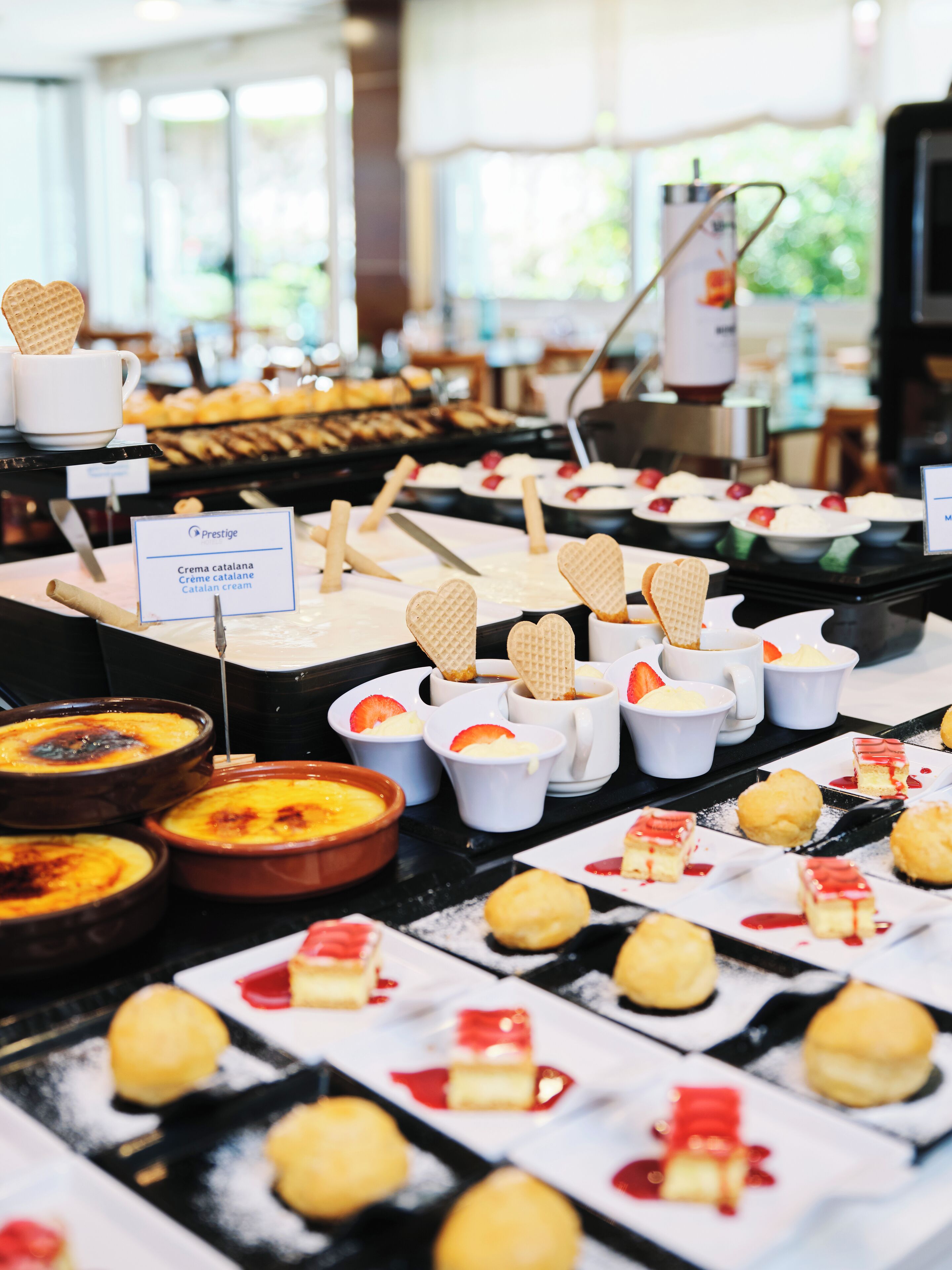 Ein Dessertbuffet mit verschiedenen süßen Köstlichkeiten und einem Schild mit der Aufschrift 'Prestige' und 'Crema catalana'.