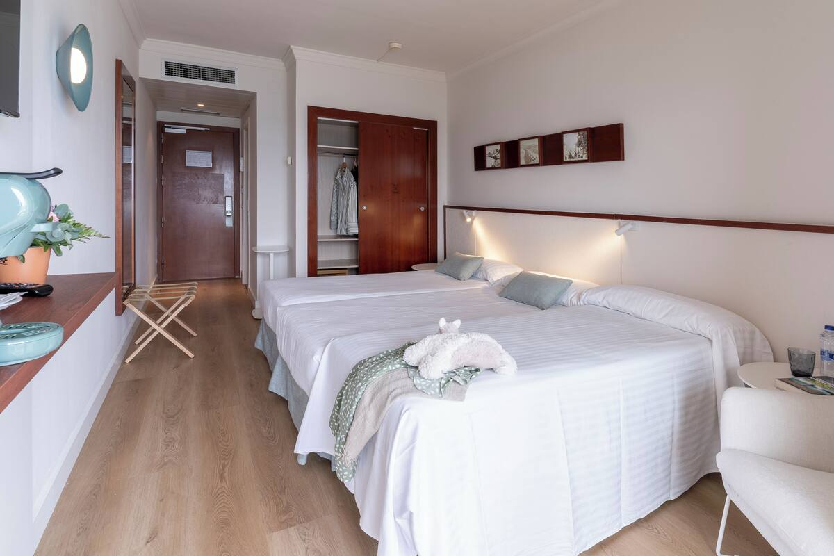 Une chambre d’hôtel avec deux lits, un bureau avec une chaise, une petite table et une armoire.