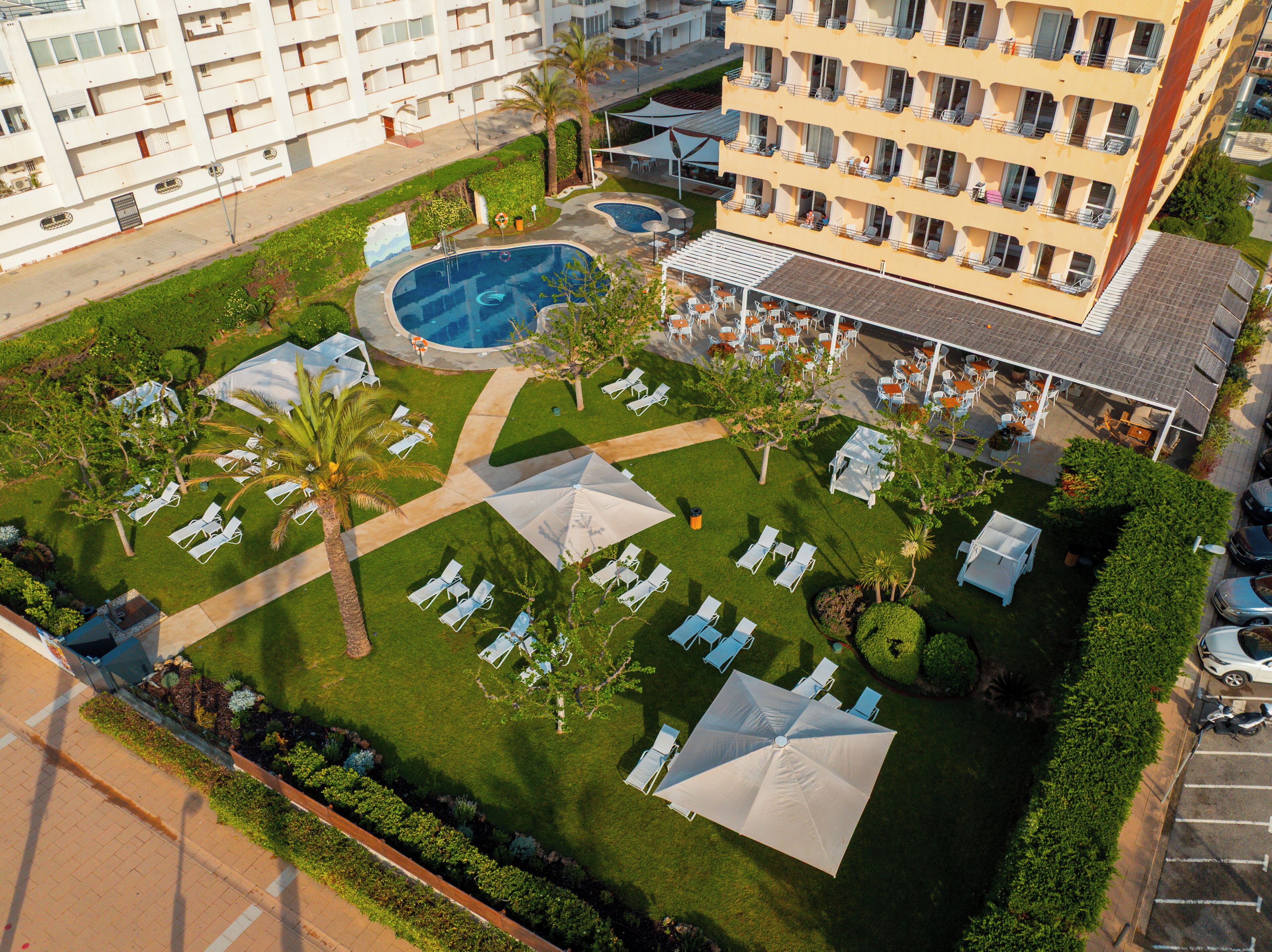 Vista aérea de un hotel con piscina, tumbonas, sombrillas y una zona de comedor al aire libre cubierta.