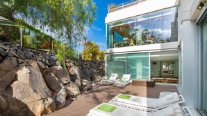 Un espace de détente extérieur moderne, avec des fauteuils en osier blanc, un mur en pierre et un bâtiment en verre en arrière-plan.