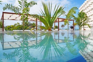 Zona de piscina con el reflejo nítido de palmeras y una estructura de edificio moderna.