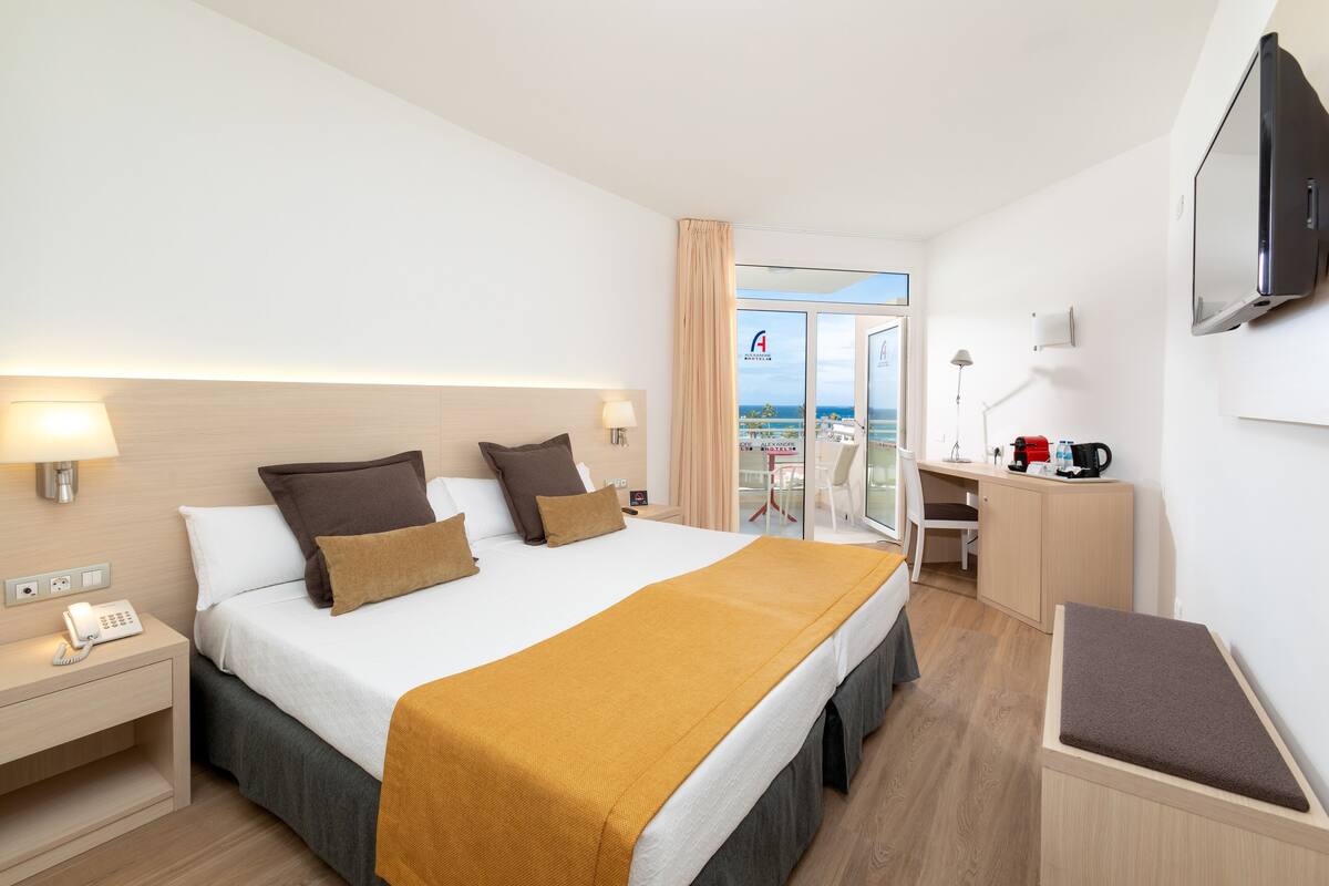 A hotel room with a bed, bedside table, lamp, desk, chair, and a TV.