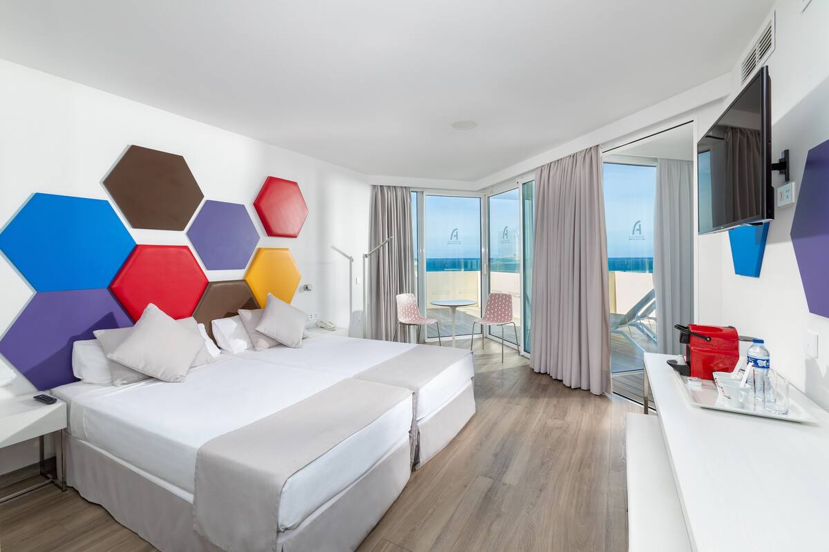 A modern hotel room with a large bed, a desk, and a view of the sea.
