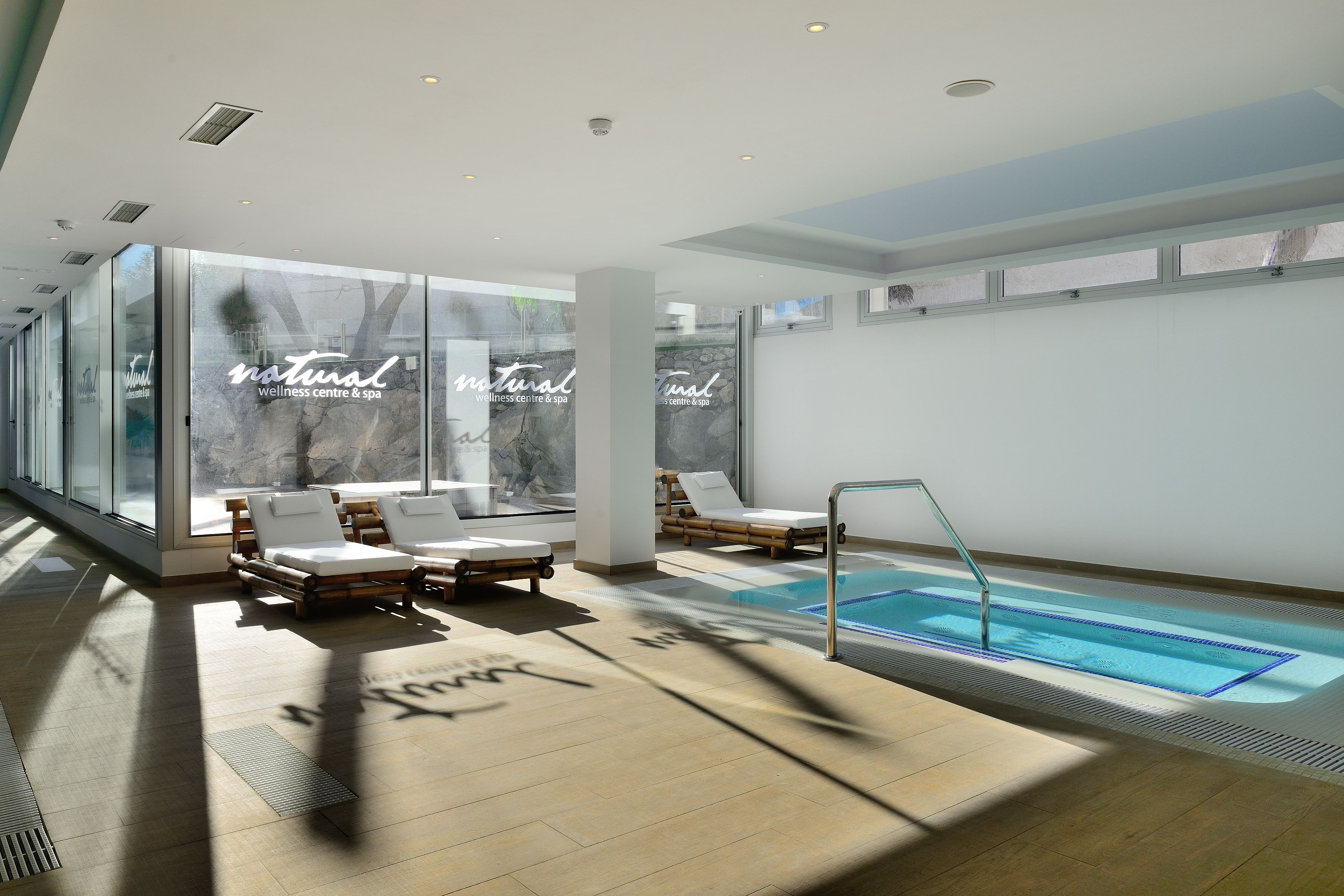 Un centre de bien-être moderne doté d’une piscine, de chaises longues et de grandes fenêtres.