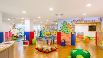 Una sala de juegos para niños con murales coloridos, mesas de juego y zonas de estar cómodas.