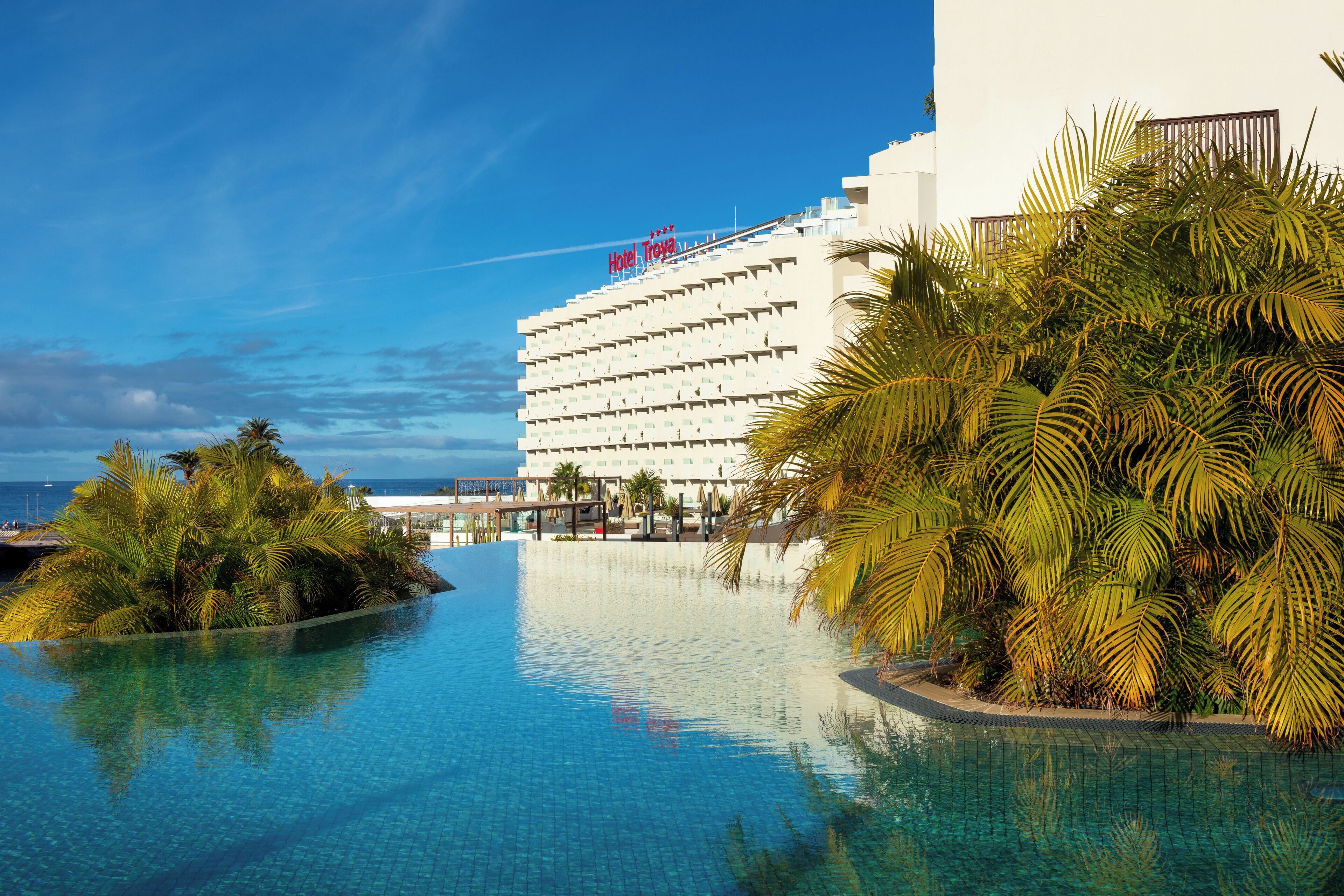 Un hotel con piscina, palmeras y vista al océano.