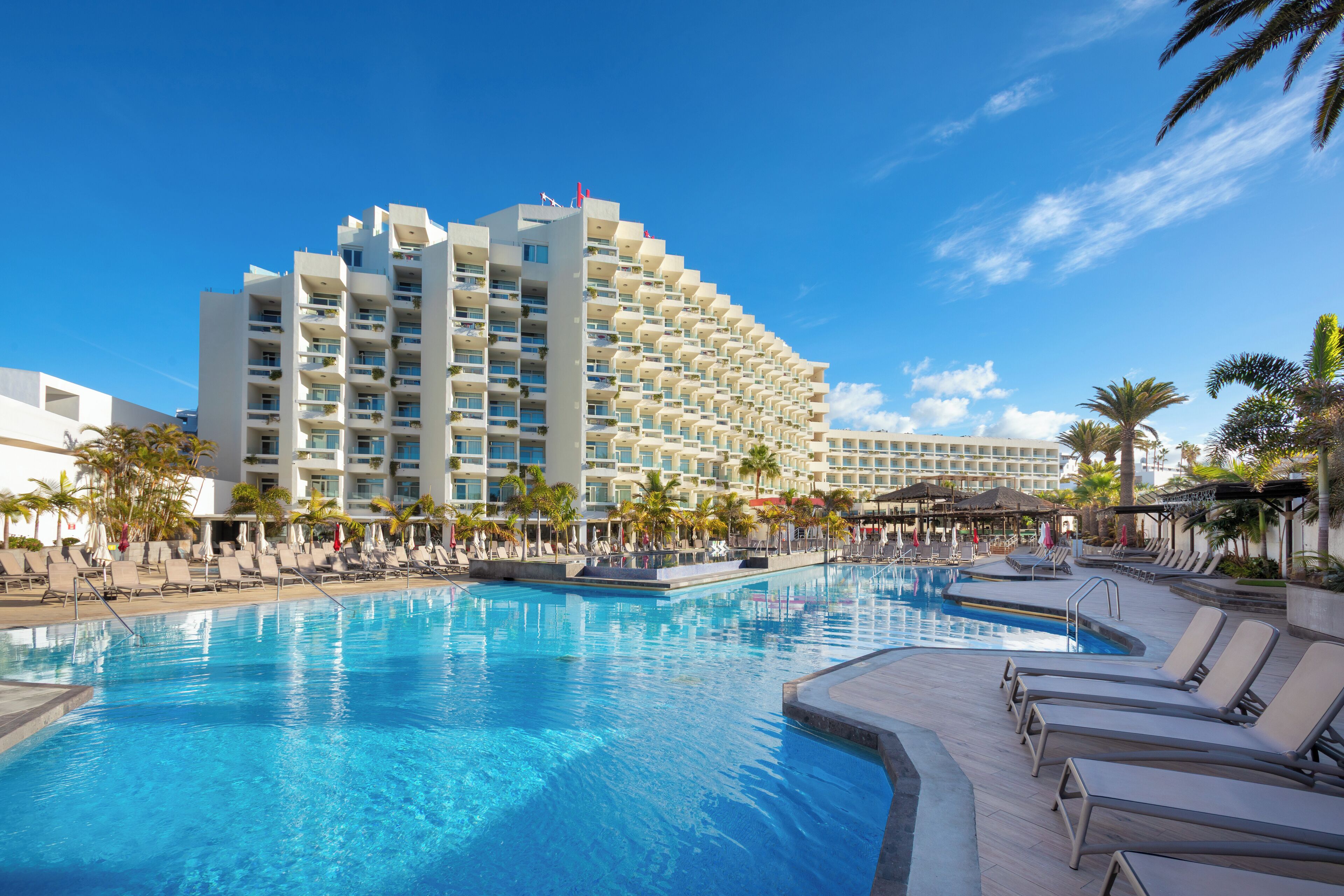 A hotel with a large pool, multiple balconies, and palm trees.