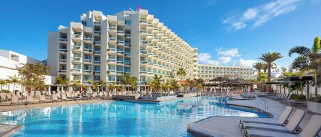 A hotel with a large pool, multiple balconies, and palm trees.